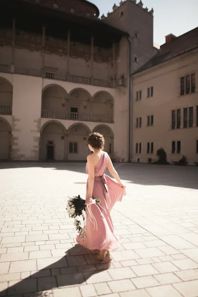 Ritratto di una bella giovane sposa che si erge tra le colonne vicino al vecchio edificio e tenendo bouquet da sposa — Foto Stock