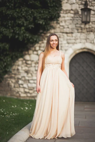 Jonge vrouw met lange jurk en haren poseren in park in de buurt van de oude poort — Stockfoto