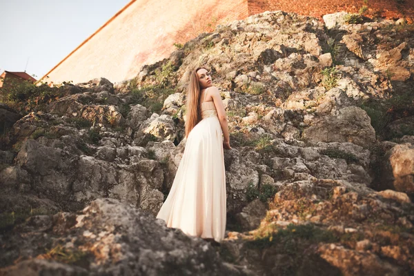 Atractiva joven en vestido largo de pie sobre las rocas — Foto de Stock