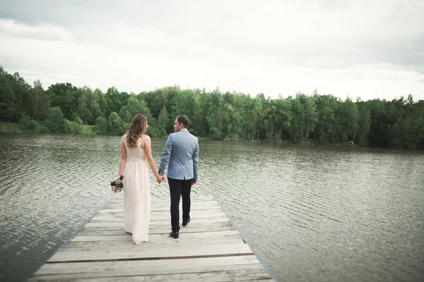 Encantadora novia, elegante novio en paisajes de montañas y puesta de sol en el lago. Hermosa pareja de boda — Foto de Stock