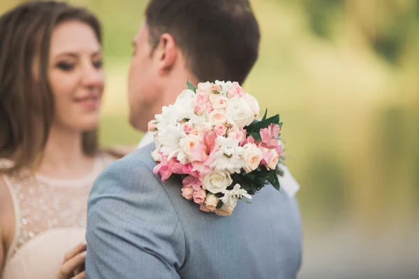 Bride and groom holding beautiful wedding bouquet. Lake, forest — Stock Photo, Image