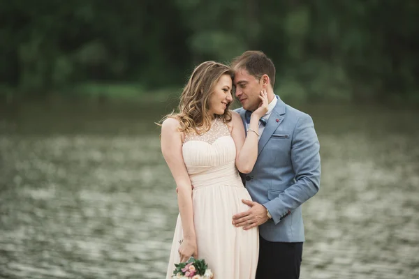 Hermosa pareja de boda, novia, novio besando y posando en el puente cerca del lago — Foto de Stock
