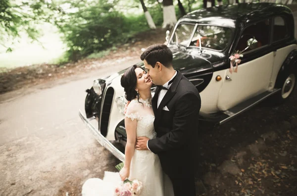 Feliz casal recém-casado, homem e mulher beijando perto de carro retro elegante — Fotografia de Stock