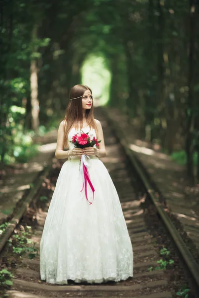 Sposa. Bella giovane donna bionda nel parco con corona di fiori e bouquet in una calda giornata estiva — Foto Stock
