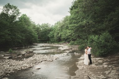 Zarif nazik şık damat ve gelin taşlarla Nehri yakınında. Evlilik çift aşık