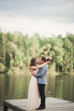 Zarif güzel düğün çifti bir göl kenarında günbatımında poz