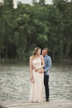 Zarif güzel düğün çifti bir göl kenarında günbatımında poz