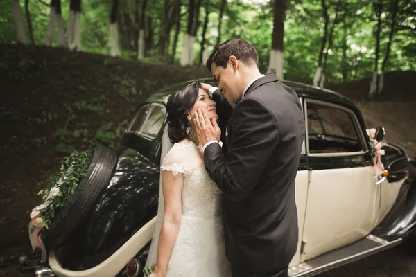 Hermosa pareja recién casada posando cerca de coche negro retro — Foto de Stock