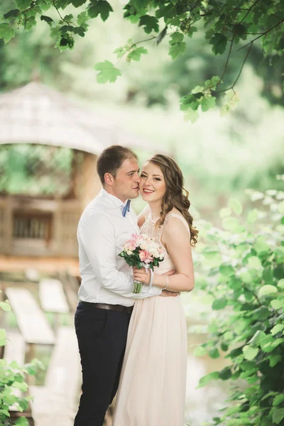 Charmant couple amoureux s'embrassant le jour du mariage, debout dans le parc en plein air près du lac — Photo