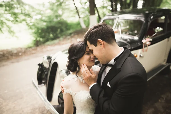 Beautiful newlywed couple posing near retro black car — Stock Photo, Image