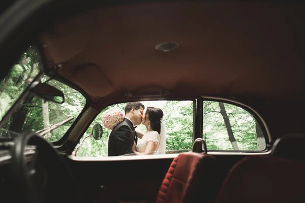 Beautiful newlywed couple posing near retro black car — Stock Photo, Image