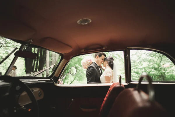 Schönes frisch vermähltes Paar posiert in der Nähe eines schwarzen Retro-Autos — Stockfoto