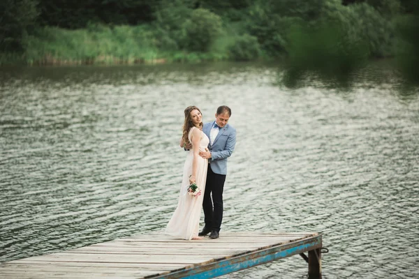 Elegante mooie bruidspaar poseren in de buurt van een meer bij zonsondergang — Stockfoto