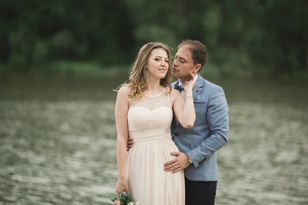 Elegante bella coppia di nozze in posa vicino a un lago al tramonto — Foto Stock