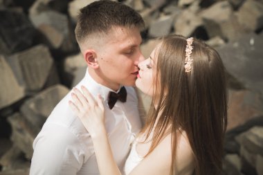 Birbirlerine aşık düğün çifti güzel manzarada kayaların yanında öpüşüyor ve sarılıyorlar.