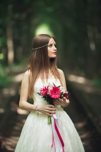 Sposa. Bella giovane donna bionda nel parco con corona di fiori e bouquet in una calda giornata estiva — Foto Stock