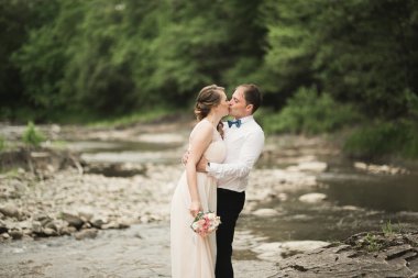 Zarif nazik şık damat ve gelin taşlarla Nehri yakınında. Evlilik çift aşık