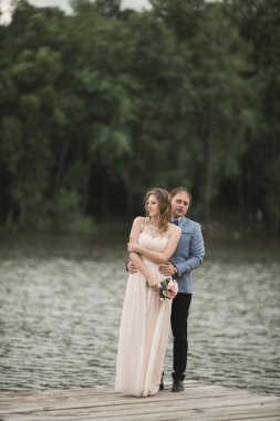 Zarif güzel düğün çifti bir göl kenarında günbatımında poz