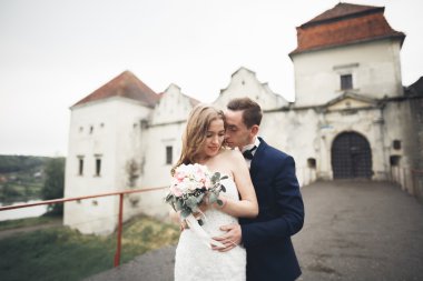 Güzel, romantik bir düğün. Yeni evliler. Eski kalenin yakınlarında sarılıyorlar.