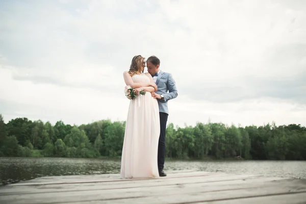 魅力的な花嫁、湖、山、夕日の風景にエレガントな新郎。豪華な結婚式のカップル — ストック写真
