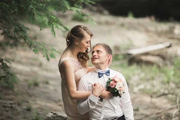 Krásný svatební pár líbání a objímání v blízkosti břehu horské řeky s kameny — Stock fotografie