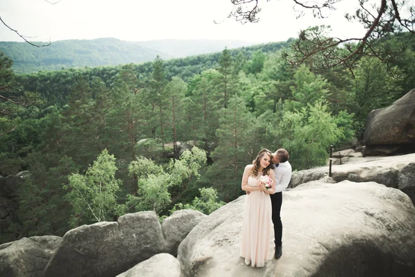 Preciosa novia, novio besándose y abrazándose cerca de los acantilados con impresionantes vistas — Foto de Stock