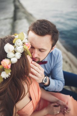 Düğün çifti mavi denizin yanındaki kayalarda öpüşüyor ve sarılıyor.