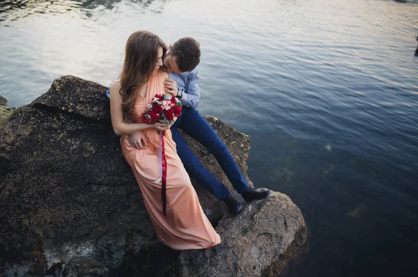 Pareja de boda sentada en piedra grande alrededor del mar azul — Foto de Stock