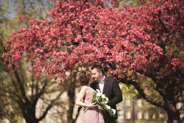 Unga bröllop par poserar nära träd med blommor — Stockfoto