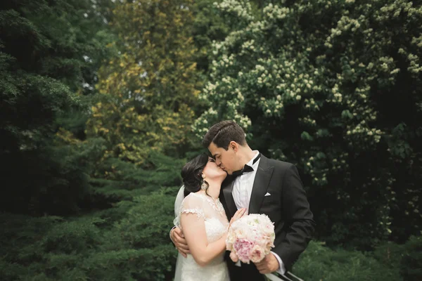 結婚式の日に公園を歩く幸せな新婚旅行のスタイリッシュなカップル花束 — ストック写真