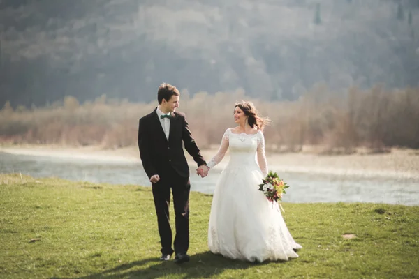 Hermosa pareja de boda, novia, novio posando y caminando en el campo sobre el fondo de las altas montañas —  Fotos de Stock