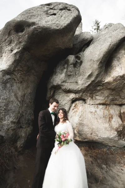 Lyckliga brudparet kyssas och kramas nära en hög klippa — Stockfoto