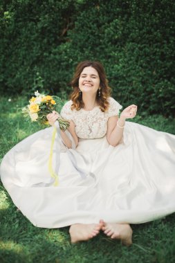 güzel gelin kameraya gülümseyen bir buket tutarak yere oturup...