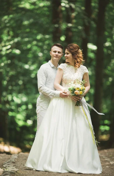 Stylish couple of happy newlyweds walking in the park on their wedding day with bouquet — Stock Photo, Image