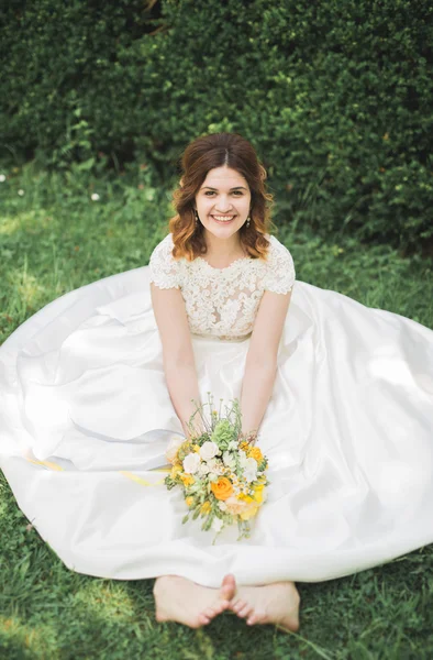 Bella sposa seduta a terra con un bouquet sorridente alla macchina fotografica — Foto Stock