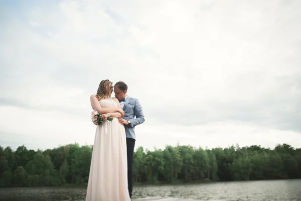 Elegante elegante novio con su hermosa novia morena feliz en el fondo de un lago — Foto de Stock