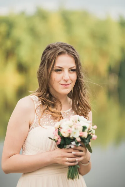 Wunderschöne Braut im eleganten Kleid mit Blumenstrauß posiert in der Nähe von Wald und See — Stockfoto