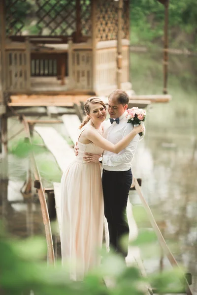 Preciosa pareja enamorada besándose en la boda del día, de pie en el parque al aire libre cerca del lago —  Fotos de Stock