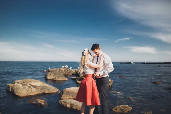 Romántica pareja amorosa posando sobre piedras cerca del mar, cielo azul — Foto de Stock