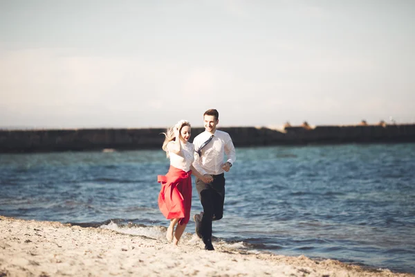 Unga lyckliga par promenader på stranden leende anläggningen runt varandra. Kärlekshistoria — Stockfoto