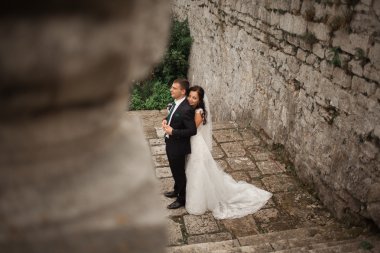 Güzel, romantik bir düğün. Yeni evliler. Eski kalenin yakınlarında sarılıyorlar.