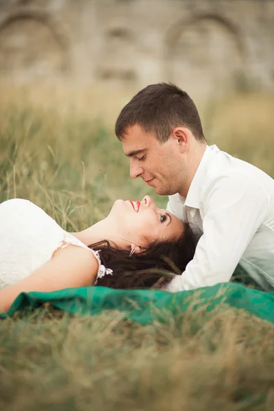 Casal de casamento feliz deitado na grama verde na hora de verão — Fotografia de Stock