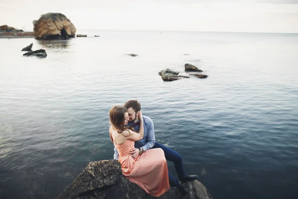結婚式のカップルの青い海とその周辺の大きな石の上に座って — ストック写真