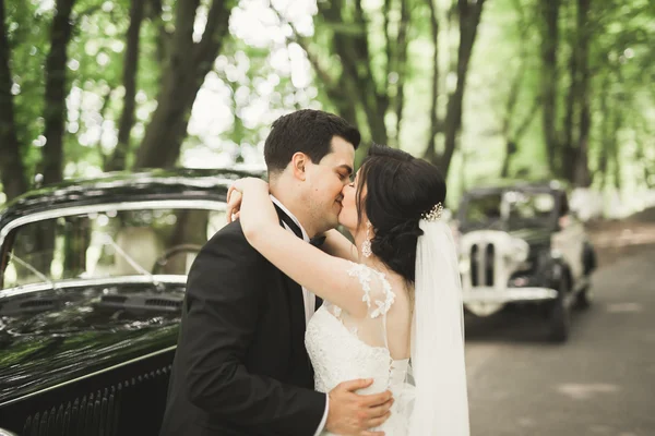 Feliz casal recém-casado, homem e mulher beijando perto de carro retro elegante — Fotografia de Stock