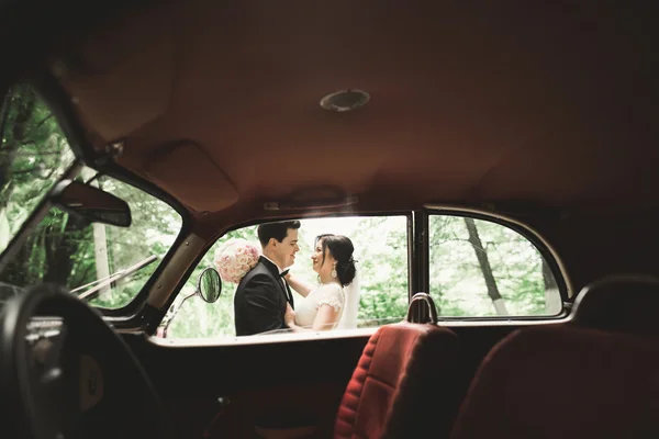 Feliz casal recém-casado, homem e mulher beijando perto de carro retro elegante — Fotografia de Stock