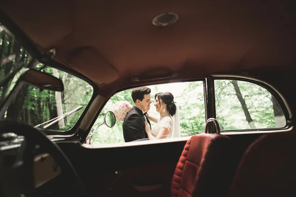 Happy newlywed couple, man and wife kissing near stylish retro car