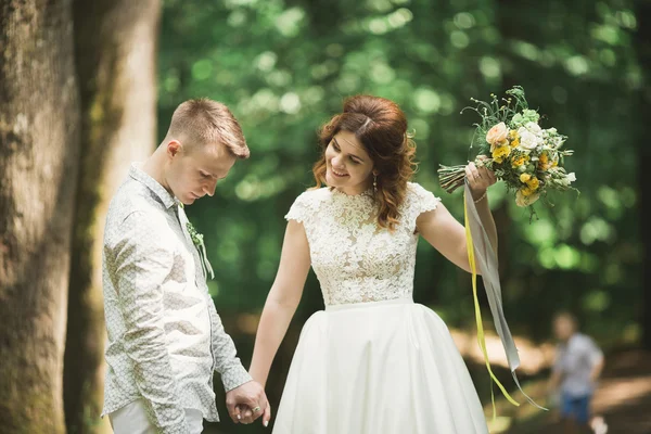 Stijlvol paar gelukkige pasgetrouwden wandelen in het park op hun trouwdag met boeket — Stockfoto