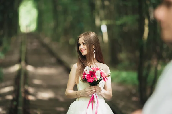 Невеста позирует и улыбается, пока жених ждет на заднем плане — стоковое фото