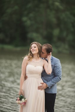 Zarif güzel düğün çifti bir göl kenarında günbatımında poz