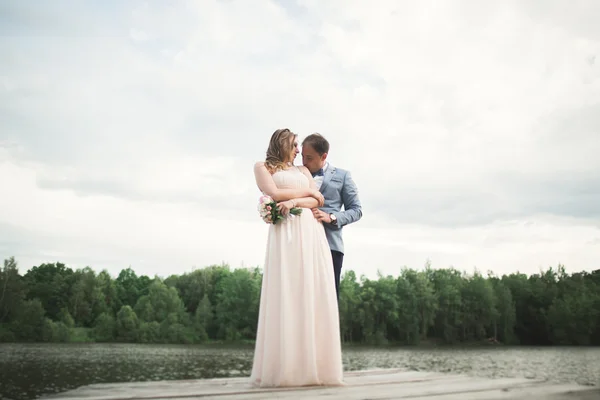 Bruid en bruidegom lopen op de rivier, lacht, zoenen — Stockfoto